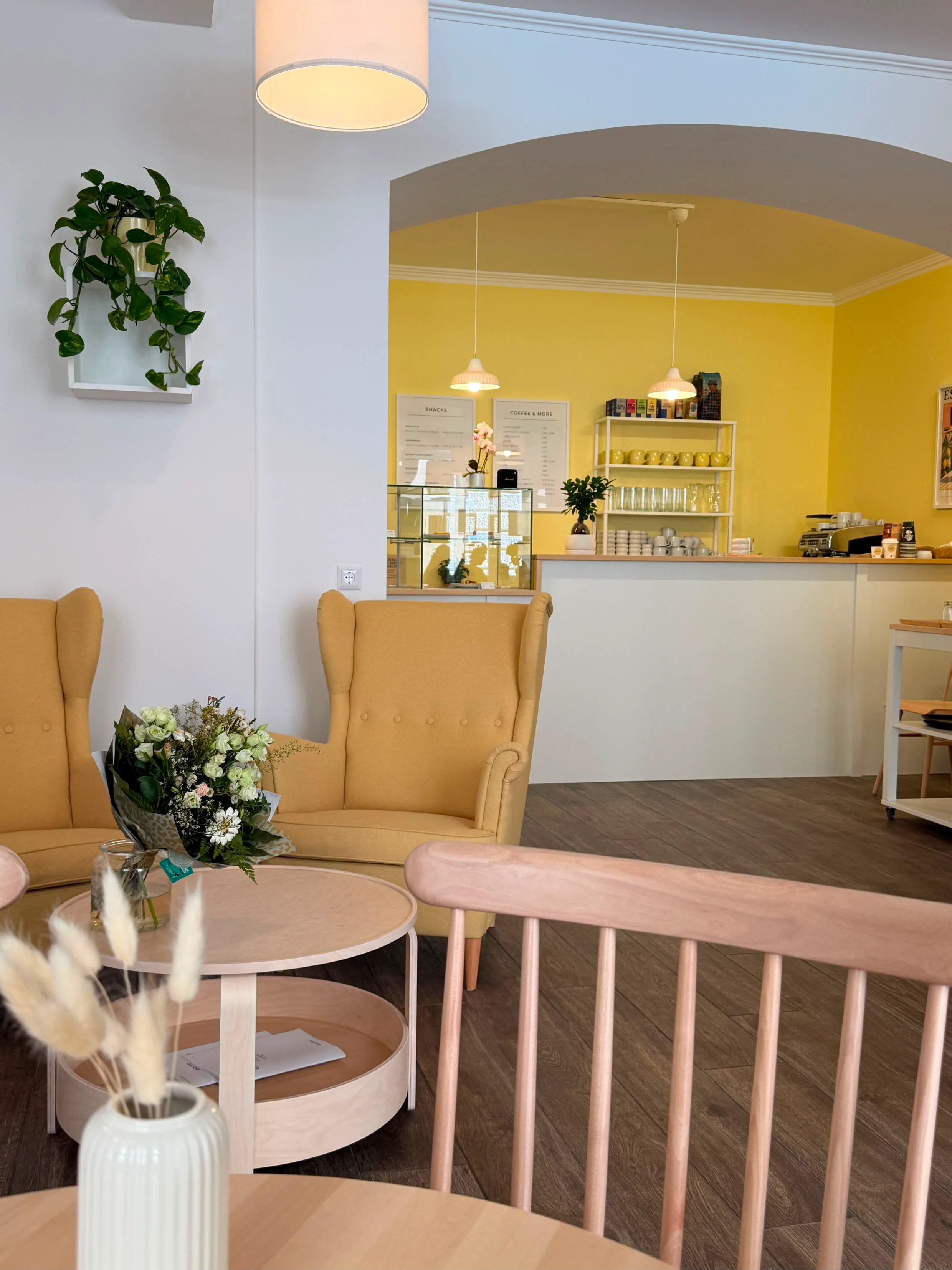 Gemütlicher Innenraum eines Cafés mit gelben Wänden, Sesseln und Kaffeebar